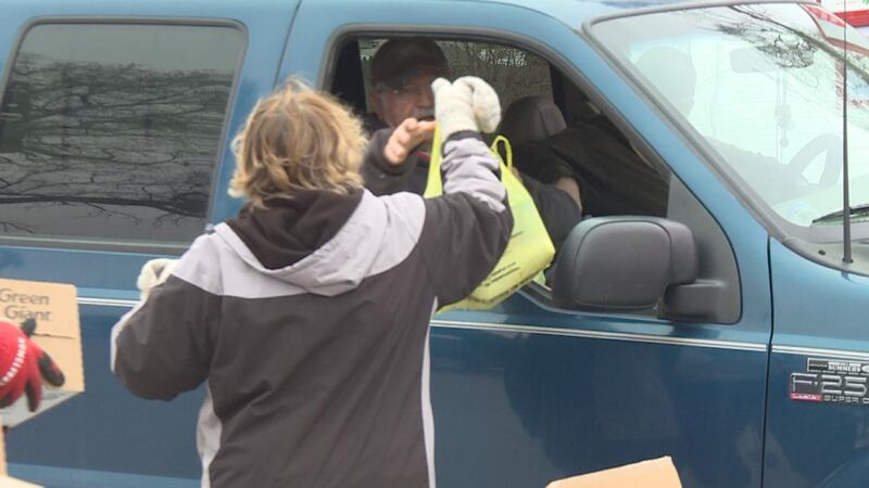 Volunteers hand out food to people in their cars. Some share jokes and kind words before...